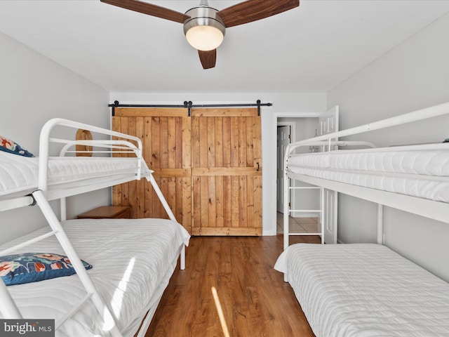 bedroom featuring a barn door, dark hardwood / wood-style floors, and ceiling fan