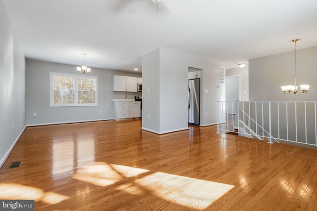 unfurnished living room featuring ceiling fan with notable chandelier and light wood-type flooring