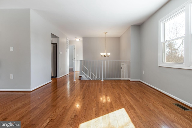 spare room featuring hardwood / wood-style floors, a healthy amount of sunlight, and a notable chandelier