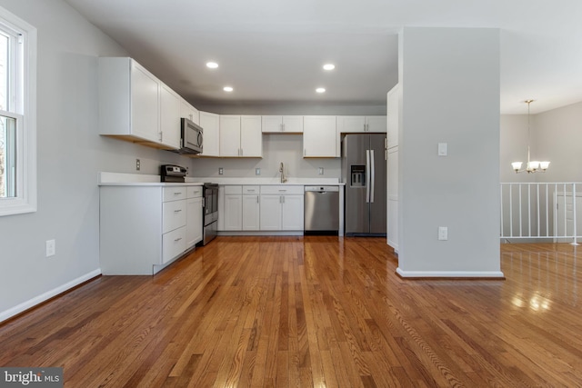 kitchen with sink, stainless steel appliances, light hardwood / wood-style flooring, decorative light fixtures, and white cabinets