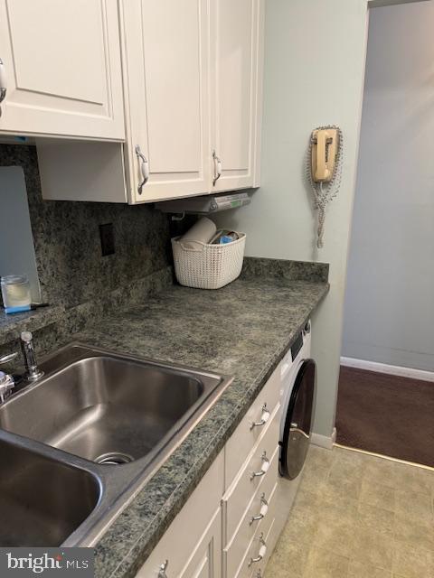 kitchen featuring washer / clothes dryer, sink, and white cabinetry