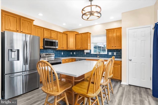 kitchen with backsplash, sink, light wood-type flooring, decorative light fixtures, and stainless steel appliances