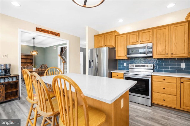 kitchen with decorative backsplash, light wood-type flooring, stainless steel appliances, and hanging light fixtures