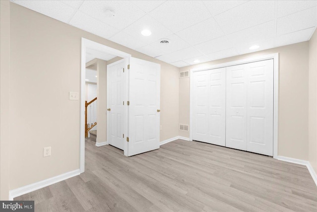 unfurnished bedroom featuring a drop ceiling, light hardwood / wood-style floors, and a closet