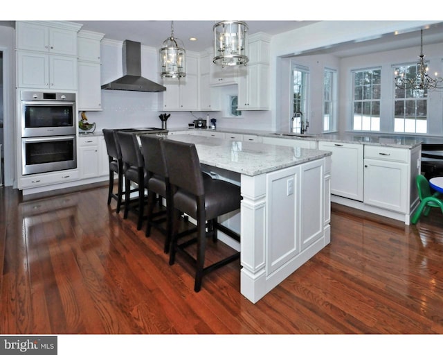 kitchen with white cabinetry, sink, wall chimney range hood, a kitchen breakfast bar, and a spacious island