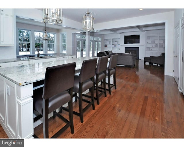 kitchen with a breakfast bar, white cabinets, decorative light fixtures, a large island, and light stone counters