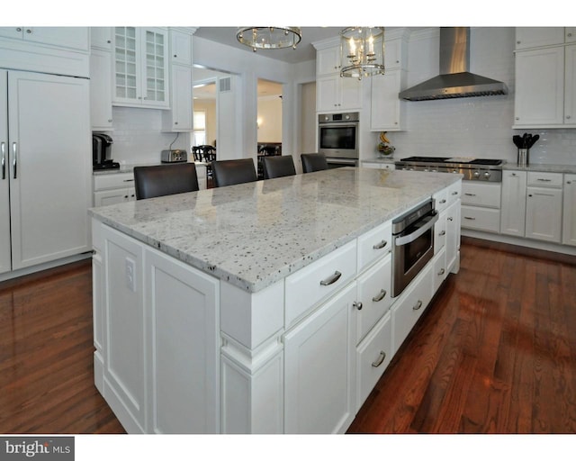 kitchen with a kitchen breakfast bar, tasteful backsplash, stainless steel appliances, wall chimney range hood, and pendant lighting