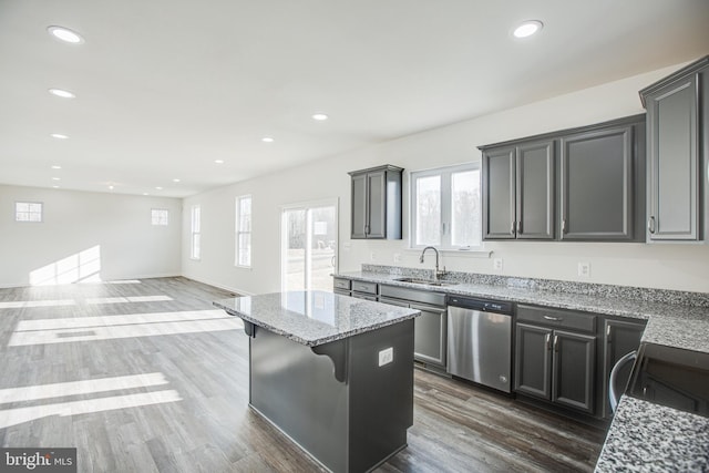 kitchen with a center island, sink, stainless steel dishwasher, light stone countertops, and a breakfast bar area