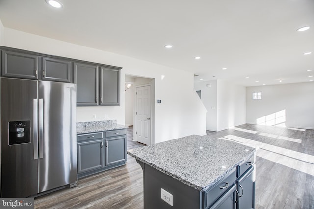 kitchen with a center island, dark hardwood / wood-style floors, stainless steel fridge, and light stone counters