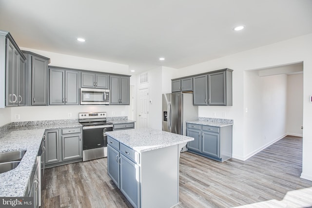 kitchen featuring gray cabinetry, a center island, light stone countertops, appliances with stainless steel finishes, and wood-type flooring