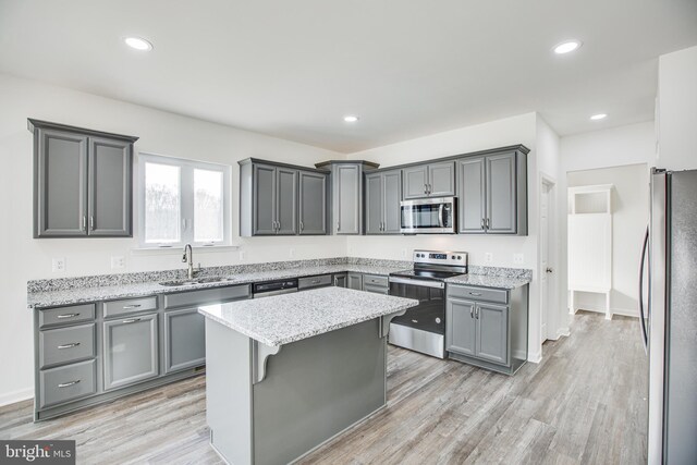 kitchen with a kitchen bar, appliances with stainless steel finishes, sink, gray cabinets, and a kitchen island