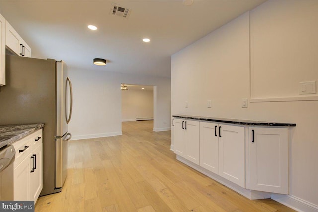 kitchen with baseboard heating, dark stone countertops, appliances with stainless steel finishes, white cabinets, and light wood-type flooring