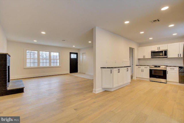 kitchen featuring a brick fireplace, white cabinets, light hardwood / wood-style floors, and appliances with stainless steel finishes