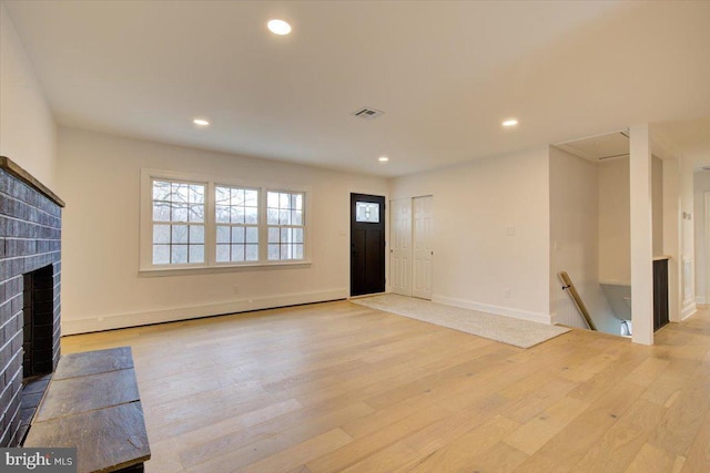 unfurnished living room featuring a fireplace, light wood-type flooring, and a baseboard heating unit