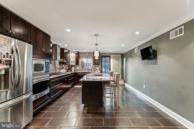 kitchen featuring a center island, a kitchen breakfast bar, wall chimney range hood, hanging light fixtures, and stainless steel appliances