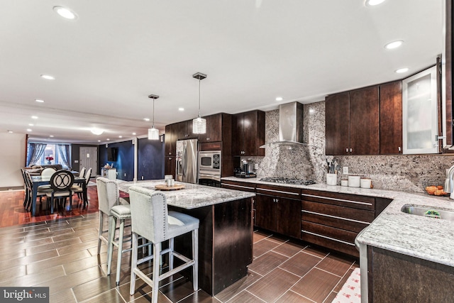 kitchen featuring hanging light fixtures, appliances with stainless steel finishes, dark brown cabinets, and wall chimney exhaust hood