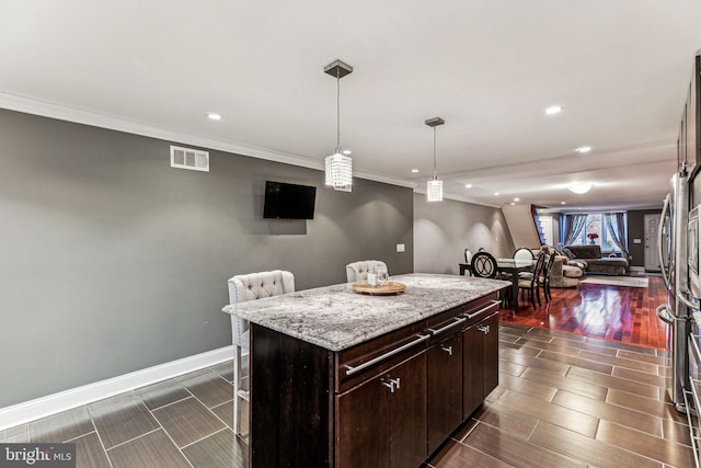 kitchen featuring ornamental molding, decorative light fixtures, a kitchen island, light stone counters, and dark brown cabinetry