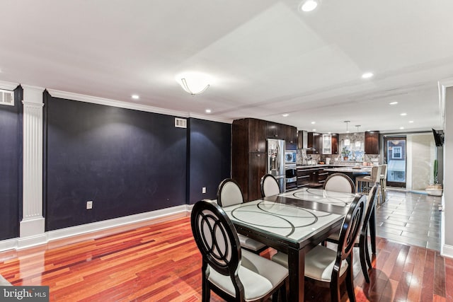 dining space with ornate columns, ornamental molding, and light hardwood / wood-style flooring