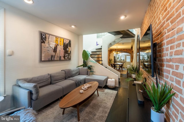 living room featuring dark hardwood / wood-style floors, brick wall, and an inviting chandelier