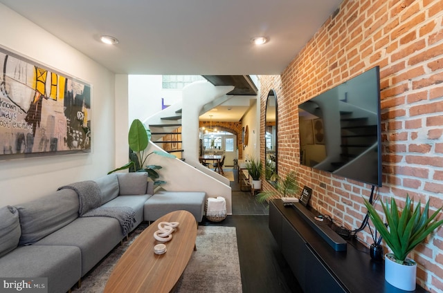 living room featuring dark hardwood / wood-style flooring, brick wall, and an inviting chandelier