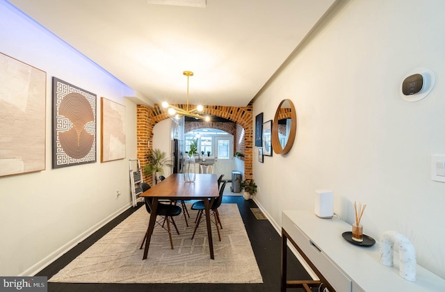 dining area featuring a notable chandelier, dark wood-type flooring, and brick wall