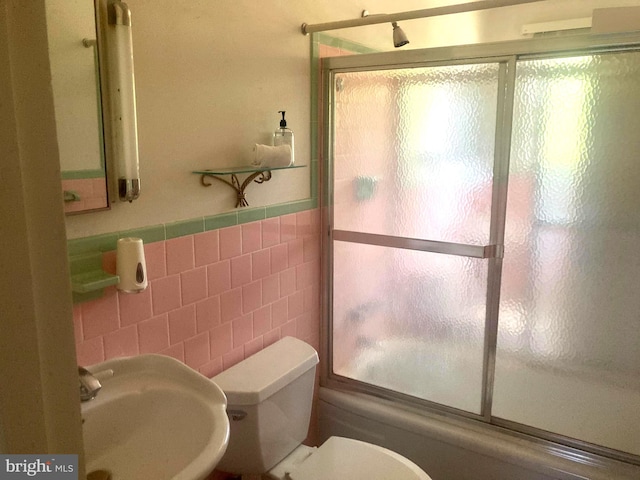 full bathroom featuring backsplash, sink, bath / shower combo with glass door, toilet, and tile walls