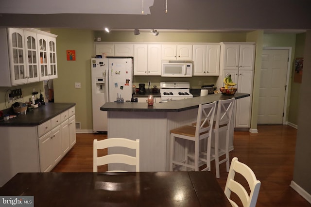 kitchen featuring dark wood-type flooring, a center island, white cabinets, and white appliances