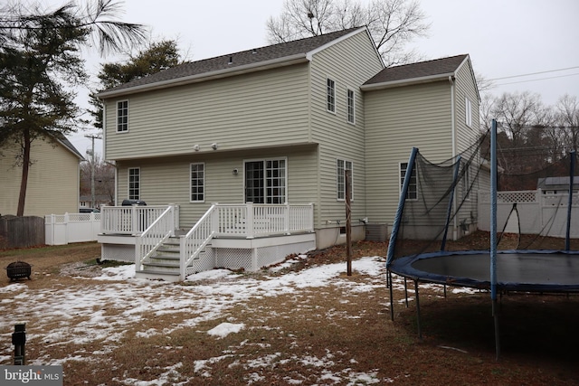 snow covered rear of property with a trampoline and a wooden deck