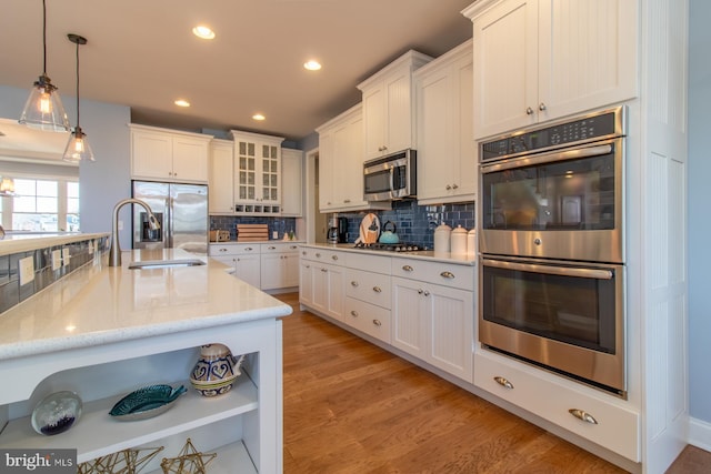 kitchen featuring white cabinets, hanging light fixtures, light hardwood / wood-style flooring, decorative backsplash, and stainless steel appliances