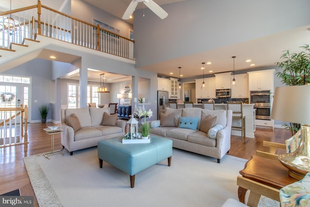 living room with ceiling fan, light hardwood / wood-style flooring, and a high ceiling