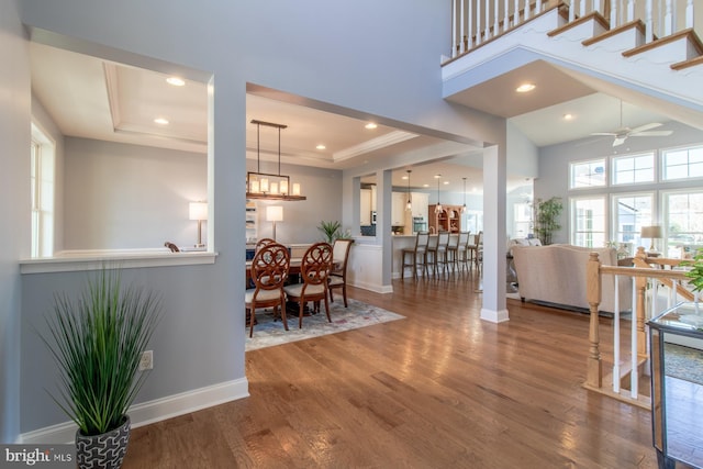 dining space with a tray ceiling, a towering ceiling, ceiling fan with notable chandelier, and hardwood / wood-style flooring