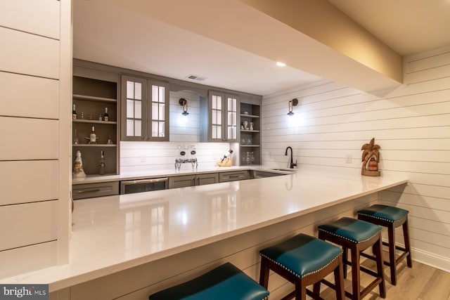 bar with wood walls, light wood-type flooring, sink, and wine cooler