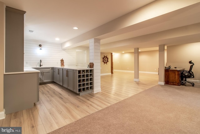 bar with light wood-type flooring, gray cabinets, and sink