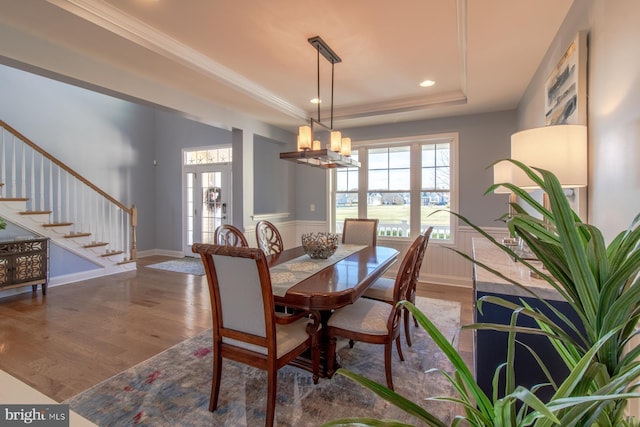 dining room featuring french doors, ornamental molding, a tray ceiling, hardwood / wood-style flooring, and a chandelier