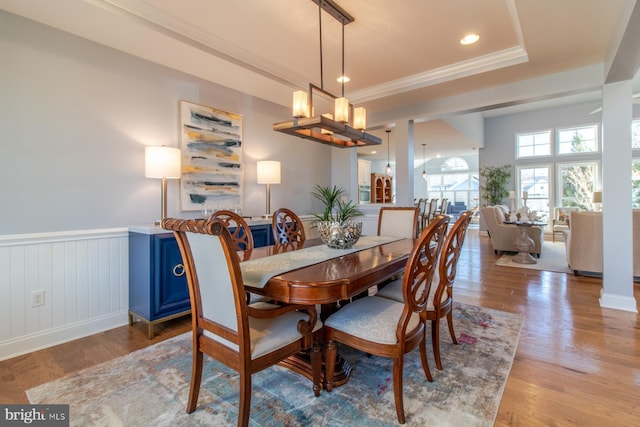 dining area featuring a raised ceiling, ornamental molding, and light wood-type flooring