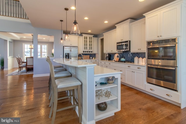 kitchen featuring a kitchen island with sink, white cabinets, hanging light fixtures, and appliances with stainless steel finishes