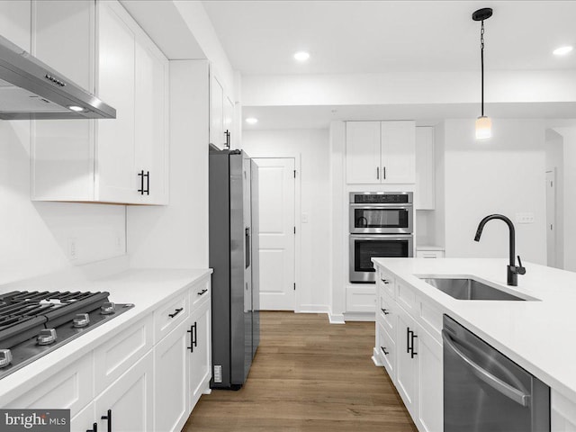 kitchen featuring wall chimney range hood, hanging light fixtures, sink, appliances with stainless steel finishes, and white cabinetry