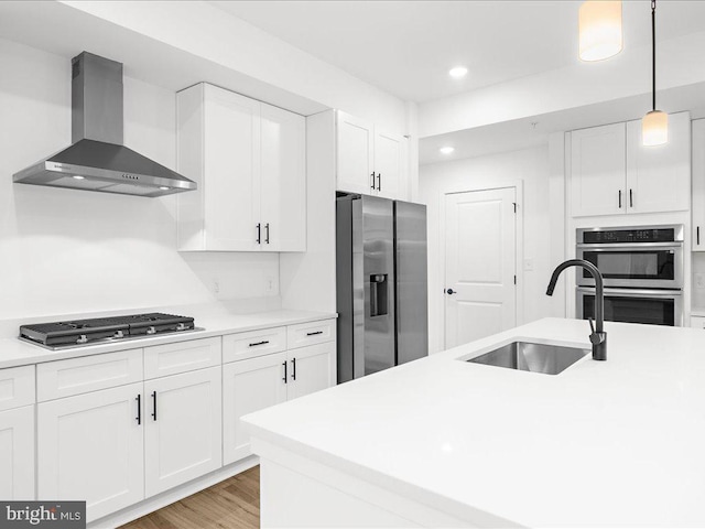 kitchen featuring sink, wall chimney range hood, decorative light fixtures, white cabinets, and appliances with stainless steel finishes