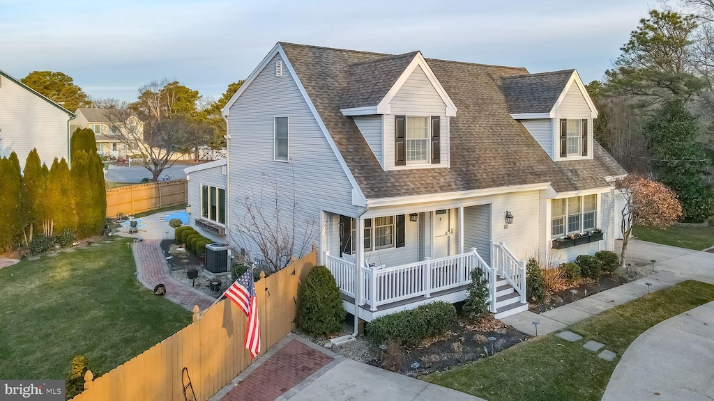 cape cod-style house featuring central AC unit, covered porch, and a front lawn