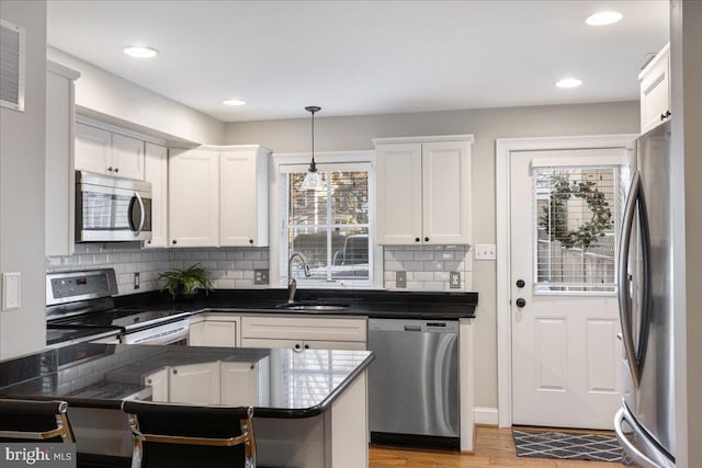 kitchen featuring kitchen peninsula, appliances with stainless steel finishes, sink, white cabinets, and hanging light fixtures