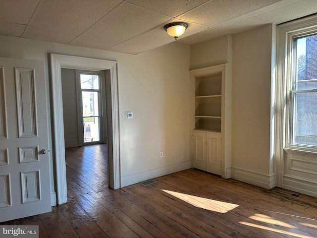 empty room with built in shelves, hardwood / wood-style floors, and a drop ceiling