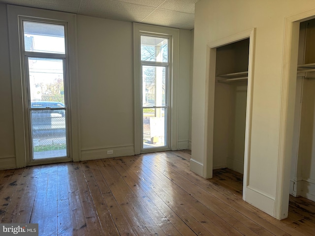 unfurnished bedroom featuring multiple windows, a drop ceiling, and hardwood / wood-style flooring