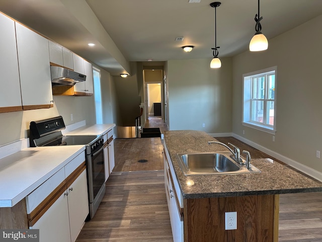 kitchen featuring stove, a kitchen island with sink, sink, decorative light fixtures, and white cabinetry