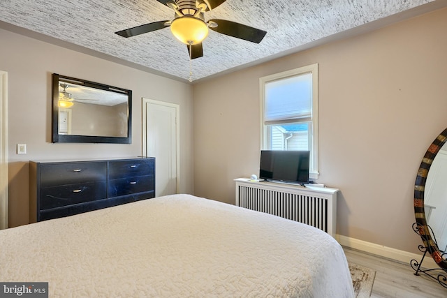 bedroom with ceiling fan, light hardwood / wood-style floors, and radiator heating unit