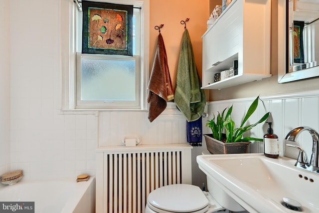 bathroom featuring a tub to relax in, radiator, sink, and toilet