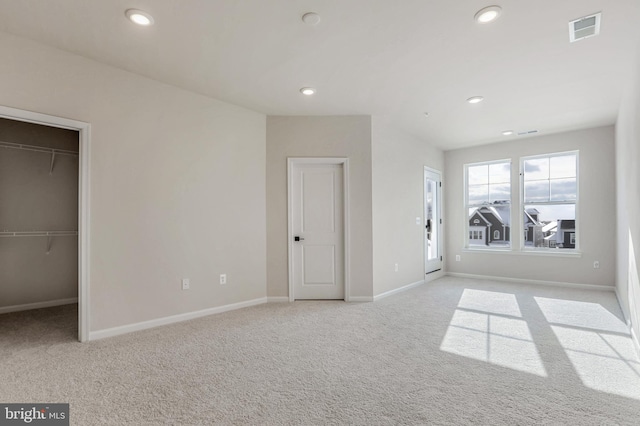 unfurnished bedroom featuring a walk in closet, a closet, and light colored carpet