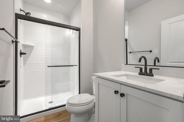 bathroom with wood-type flooring, vanity, toilet, and a shower with shower door