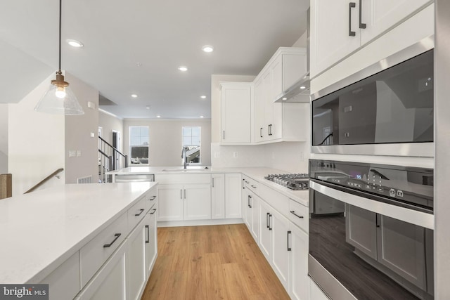 kitchen with sink, light hardwood / wood-style flooring, appliances with stainless steel finishes, decorative light fixtures, and white cabinetry