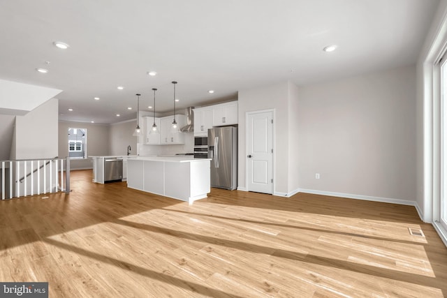 kitchen featuring appliances with stainless steel finishes, light wood-type flooring, pendant lighting, a center island, and white cabinetry