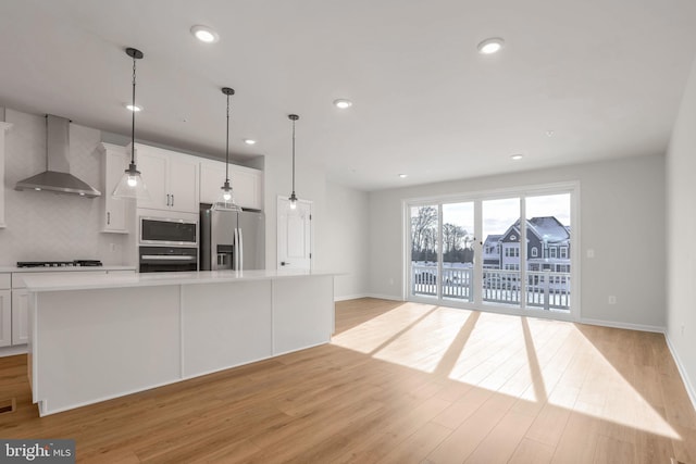 kitchen featuring stainless steel appliances, wall chimney range hood, backsplash, a spacious island, and white cabinets